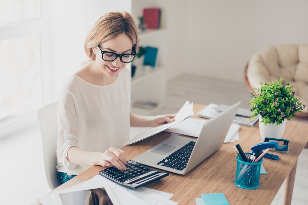 A woman works from home and smiles at her desk.