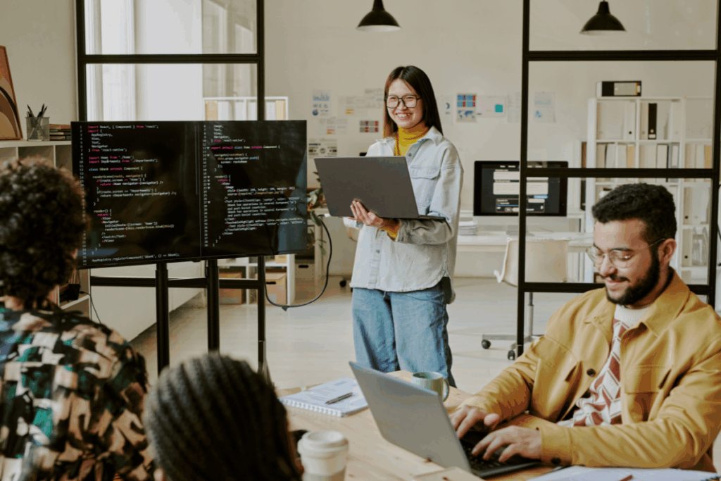 A development team takes part in a meeting. One woman stands forward and presents her code to the room.
