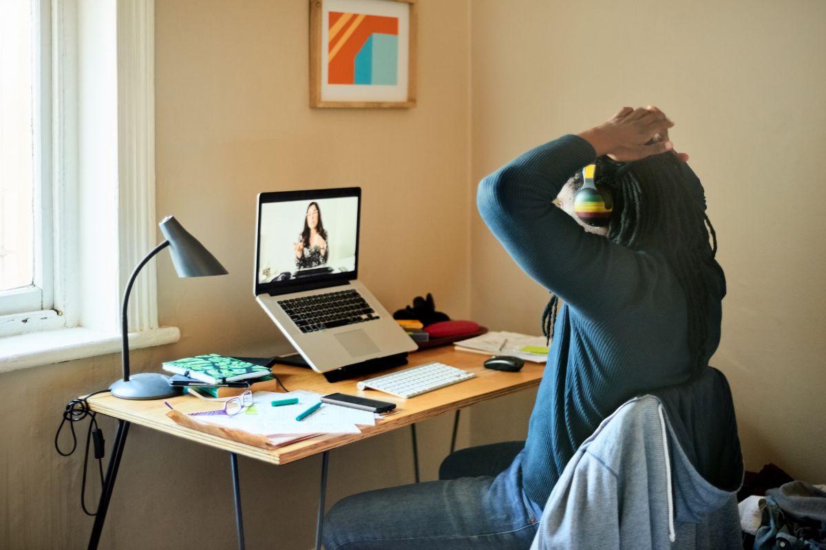 A woman works from home. She is in a remote onboarding session. She is wearing headphones and there are notebooks and pens on her desk