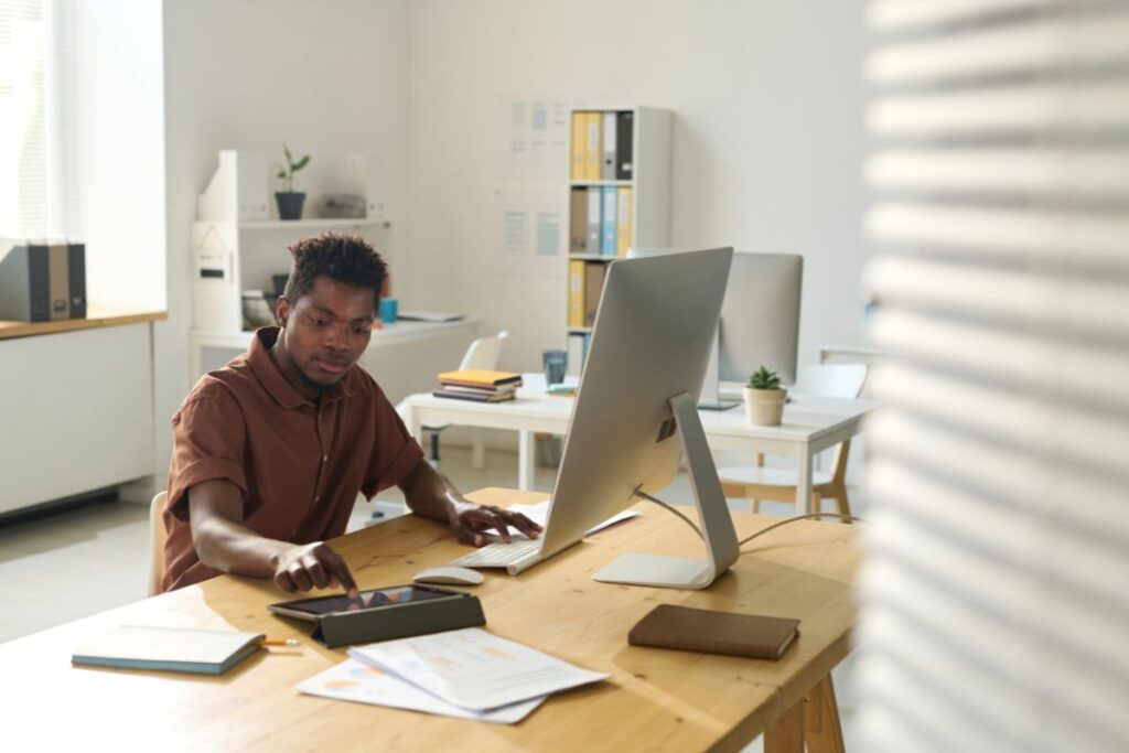 A man works remotely in his kitchen. He scrolls on a tablet. 