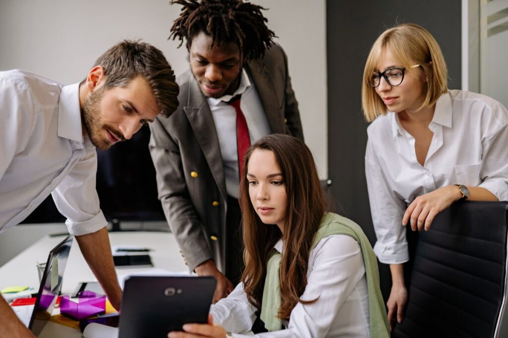 A group of four employees collaborate on a project over a tablet.